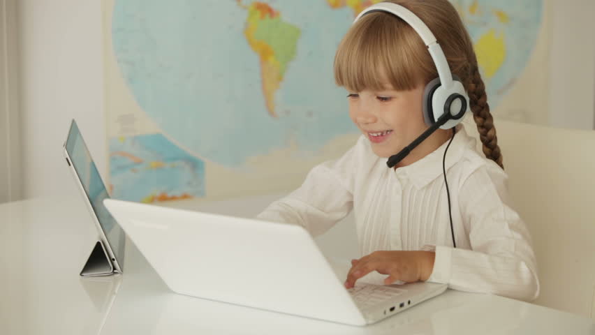 Beautiful little girl wearing headset sitting at table working on laptop and