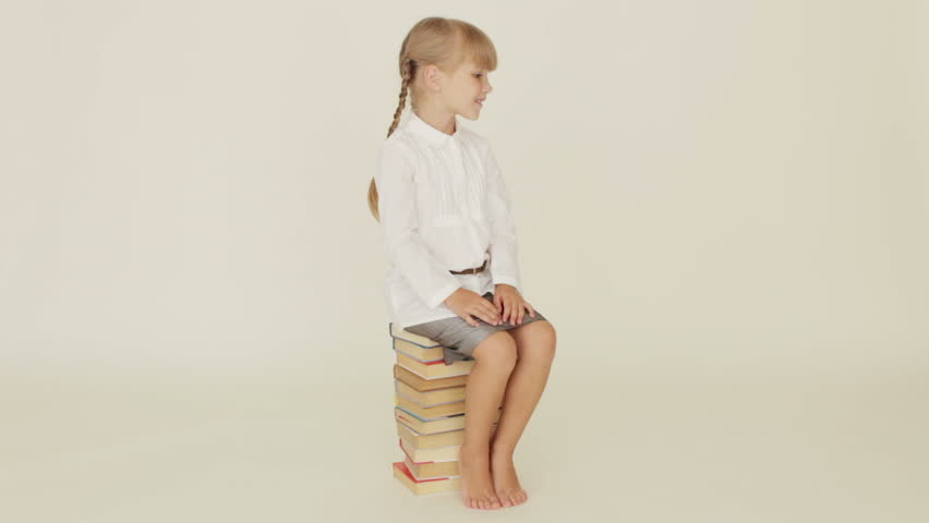 Cute little girl sitting on pile of books and smiling at camera