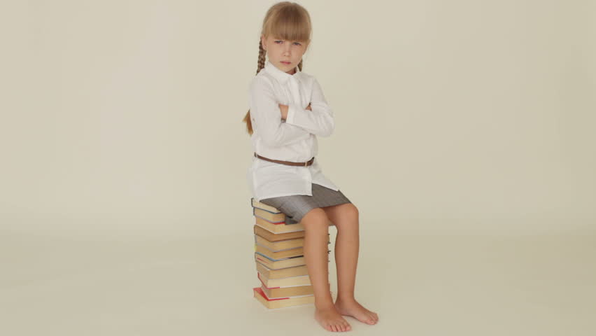 Funny little girl expressing discontent sitting on pile of books and shaking her