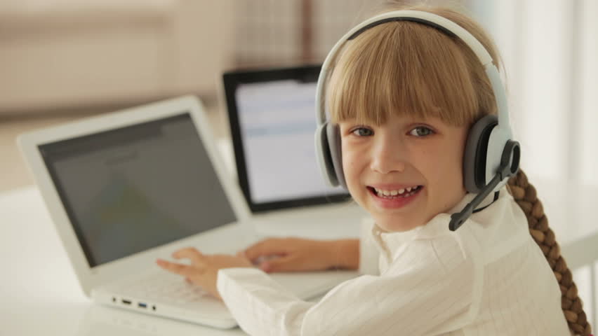 Funny little girl in headset with microphone using laptop and touchpad laughing