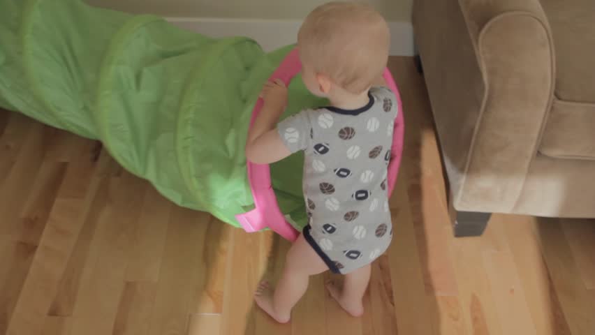 A baby boy playing with a green tunnel in his house.