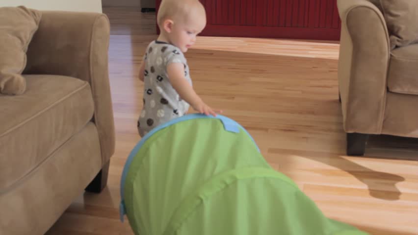 A baby boy playing with a green tunnel in his house.