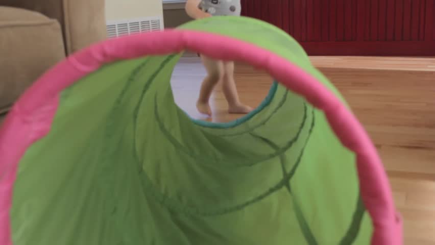 A baby boy playing with a green tunnel in his house.