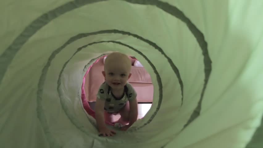 A baby boy playing with a green tunnel in his house.