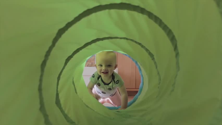 A baby boy playing with a green tunnel in his house.