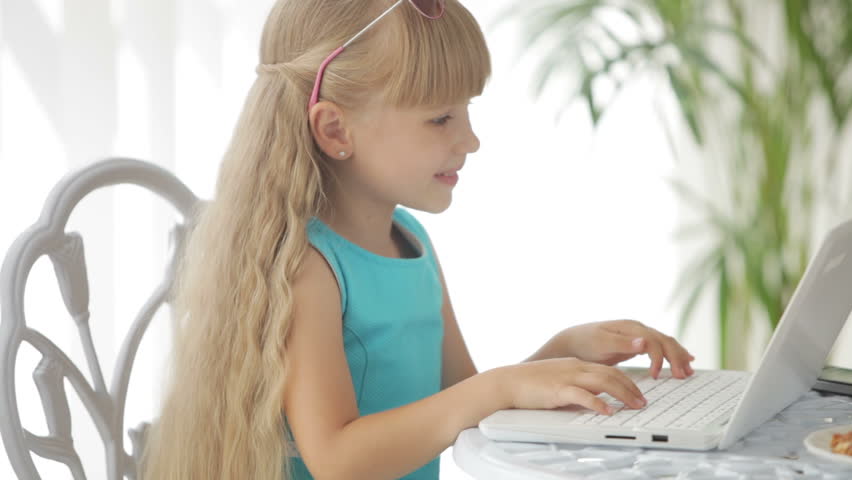 Pretty little girl sitting at table laughing and using laptop