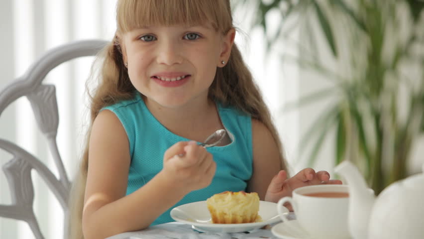 Pretty little girl sitting at table eating cake and smiling at camera