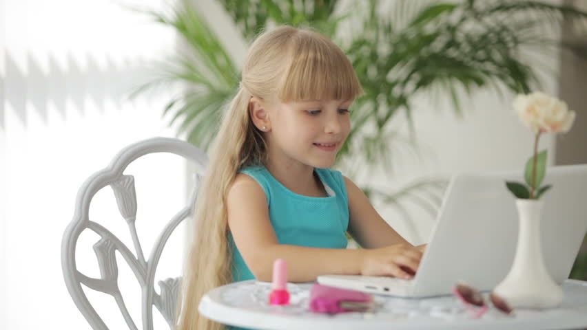 Funny little girl sitting at table with laptop in front of her and painting her
