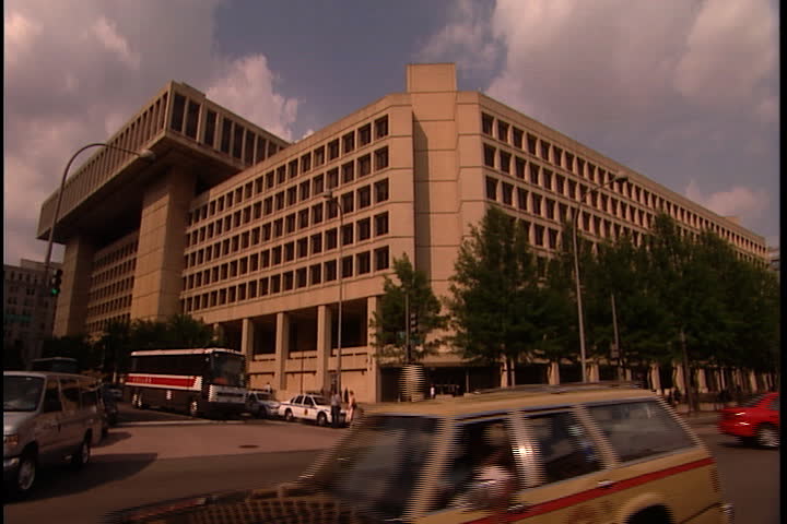 WASHINGTON, D.C. - MAY 29, 2002: LS exterior of the J. Edgar Hoover FBI Building, framed by blue sky and white fluffy clouds: traffic on busy intersection in the foreground.