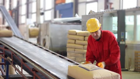 Worker controls sacks of sugar on the conveyor belt in a sugar factory