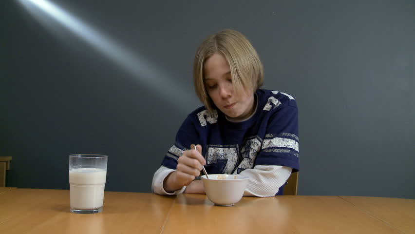 Teenager sitting at table eating noodles from a bowl.  Glass of milk on table
