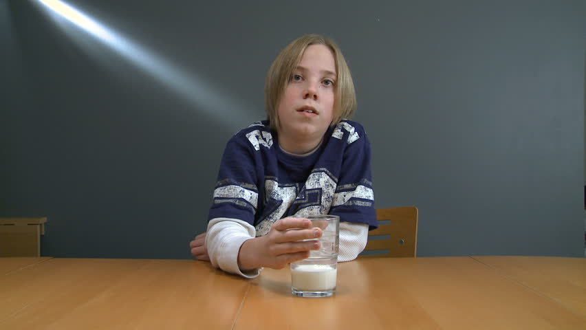 Teenager sitting at table, finishing a glass of milk.