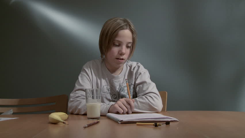 Teenager finishing a homework assignment and drinking a glass of milk.