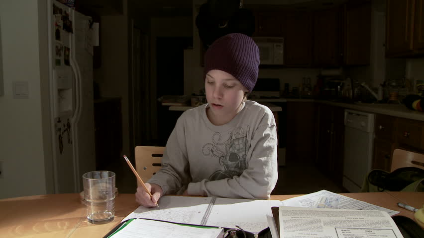 Teenager working on a homework assignment with kitchen in background.