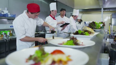 Professional chefs in a restaurant or hotel kitchen. They are looking at a digital tablet and organizing their menu and work schedule.