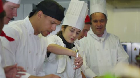Mixed ethnicity team of professional chefs preparing and cooking food in a commercial kitchen. The head chef tastes a dish and gives his approval.