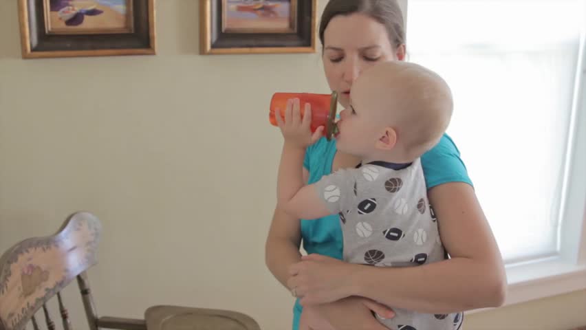A baby drinking from a cup while being held by his mother