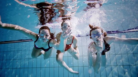 Young female friends in a swimming pool having fun together underwater and blowing kisses to the camera.