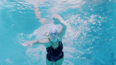 View from underneath of a professional female swimmer underwater with a bright light reflecting against the surface of the water.