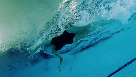 View from underneath of a professional female swimmer underwater with a bright light reflecting against the surface of the water.