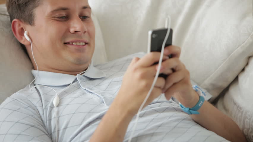 Handsome young man lying on sofa listening to music with earphones and smiling