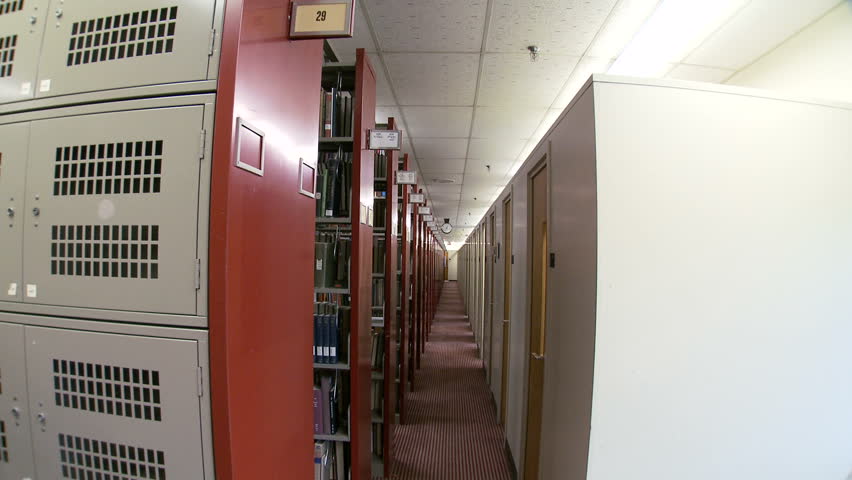 Following a woman from behind as she walks past the stacks in a library.