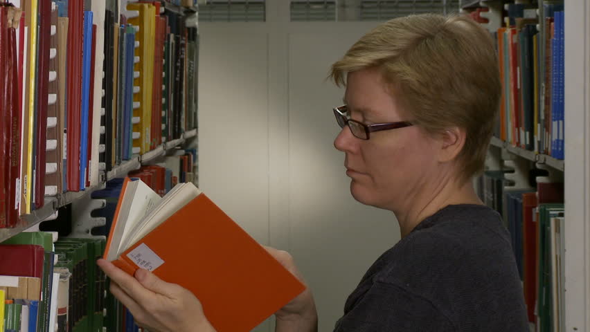 Close up of woman finding an orange book on library shelves.