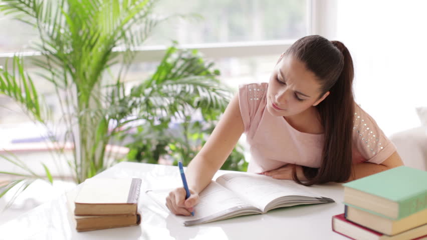 Pretty student girl studying at table with books