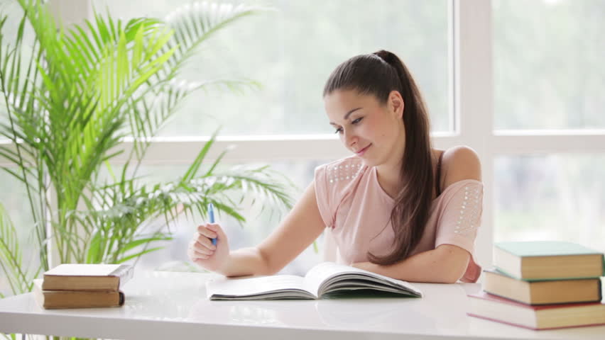 Pretty student girl studying at table with books and smiling at camera