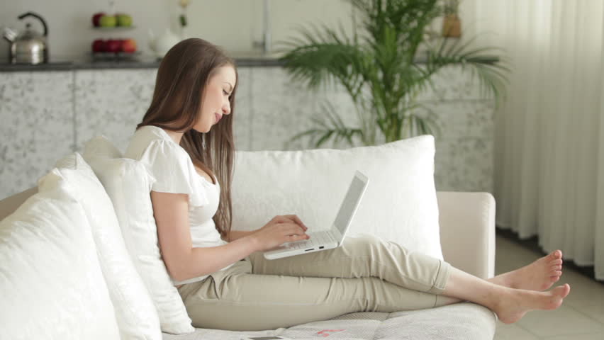 Charming young woman sitting on sofa with laptop and credit card and smiling