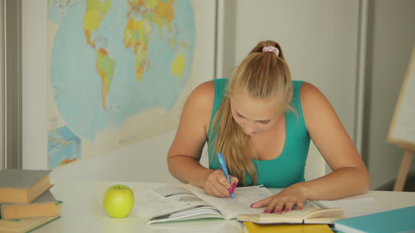 Young girl sitting at table writing and eating apple