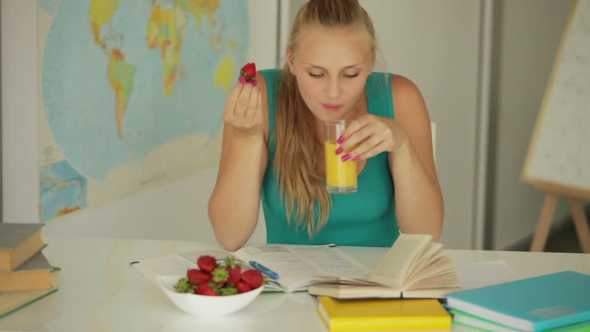 Young girl sitting at table eating strawberry and drink juice