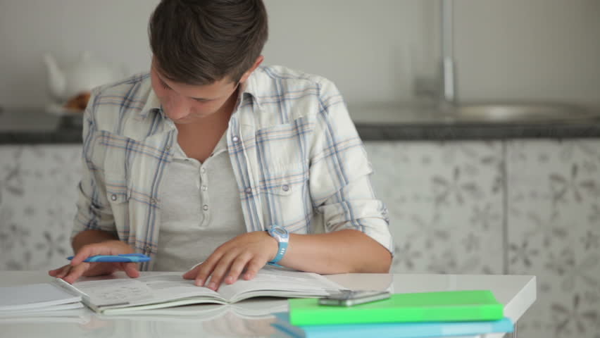 Good-looking guy studying at table writing in notebook and smiling at camera