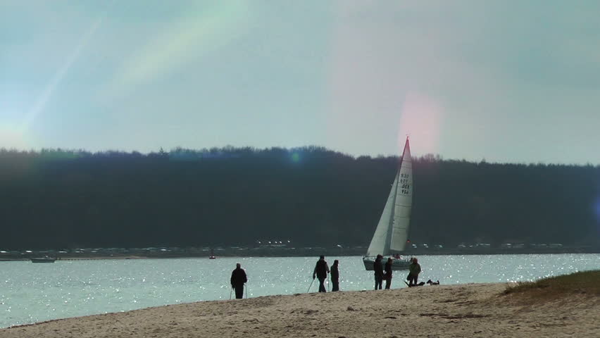 People walking on the beach and yacht passing by at sunset