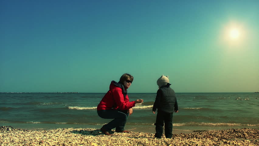 Mother teaching her son to throw sea shells