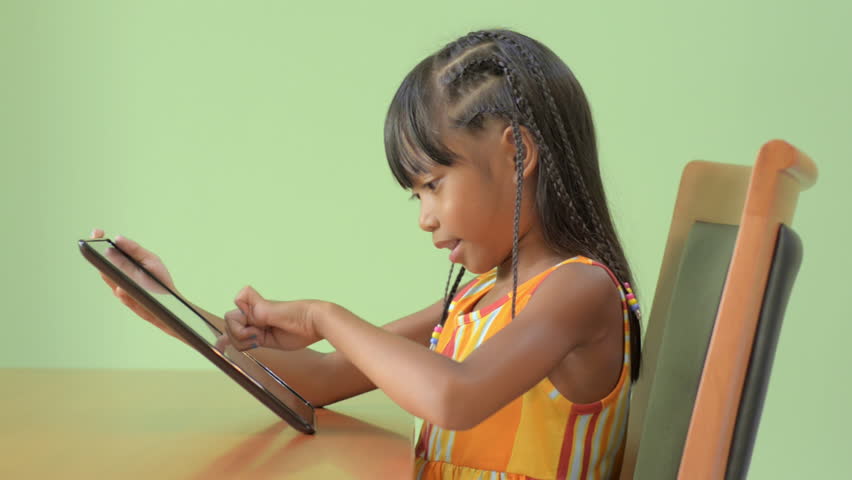 A cute Asian girl smiling and happily playing on a tablet pc. 
