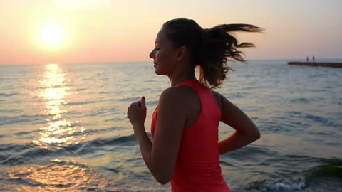 a young woman with a slender figure is engaged in gymnastics at sea at sunrise. She makes a run along the sea coast. sequence camera stabilizer shots. 