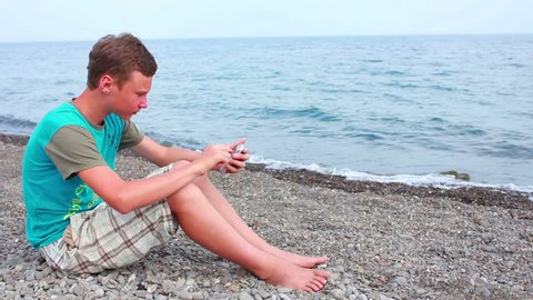 boy playing on the seashore smartphone
