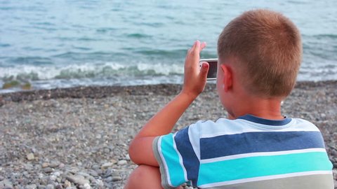 boy playing on the seashore smartphone

