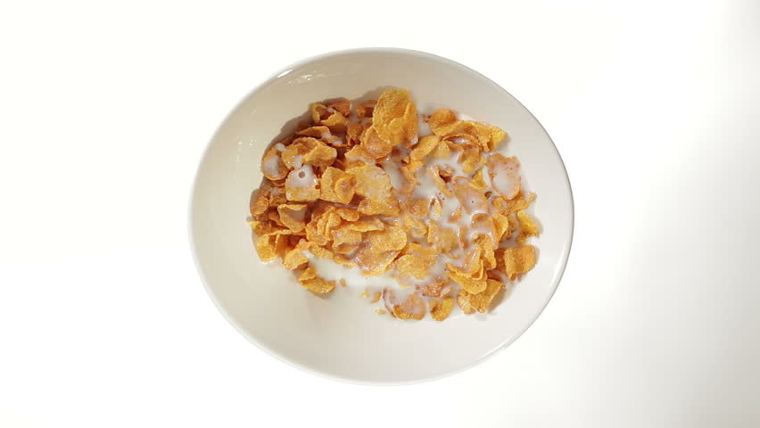 Hand mixing a bowl of cornflakes and milk with a spoon on white background