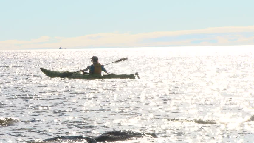 Woman kayaker paddles along Lake Superior in Minnesota on sunny day.