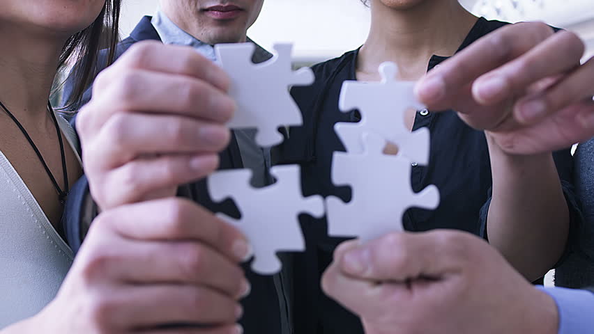 Making the pieces fit. Business people bring jigsaw puzzle together.