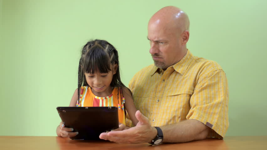 A cute young Asian girl walks in and takes an ipad from her busy father.