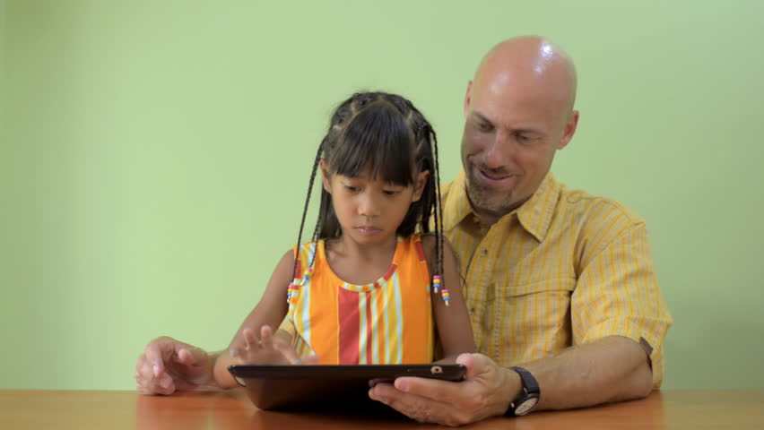 A father and his Asian daughter enjoying using a tablet computer together,