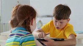 Boy using a digital tablet, girl watching him then turning and smiling at camera, shifting focus