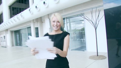 Ecstatic businesswoman celebrates her success and throws papers and documents into the air in the middle of a busy contemporary office building. High quality HD video footage