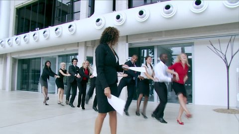 Happy multi ethnic business team dance in a congo line through a large contemporary corporate building. High quality HD video footage