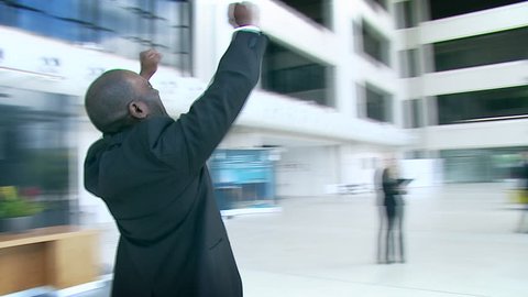 Ecstatic businessman celebrates his success and throws papers and documents into the air in the middle of a busy contemporary office building. High quality HD video footage