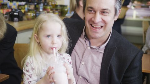 Cute little girl in a cafe, shares her milkshake with her father or family member. In slow motion. Video de stock