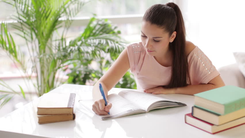 Cheerful student girl studying at table with books and smiling